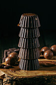 Appetitanregende Pralinen aus dunkler Schokolade, übereinander gestapelt und auf einem Holzbrett vor schwarzem Hintergrund serviert