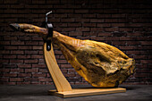 Delicious dry cured Spanish pork leg on wooden holder on gray surface