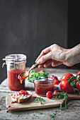Unbekannte ältere Frau, die beim Mittagessen mit einem Löffel frische Tomatenmarmelade auf Brot streicht, vor schwarzem Hintergrund