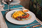 Plate with yummy grilled octopus garnished with sliced potatoes and dry paprika near sauce on served table