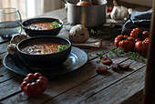 Komposition aus servierten Schalen mit köstlicher Tomatencremesuppe mit Kernen auf einem Tisch mit Tomaten und Brotbrötchen