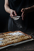 Crop shot of woman covering freshly baked frangipane apple pie with powdered sugar on wooden table