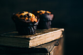 Chocolate muffins on an old book over a dark background