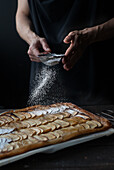 Crop shot of woman covering freshly baked frangipane apple pie with powdered sugar on wooden table