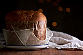 Ungeschnittener, frisch gebackener, handwerklich hergestellter Weihnachts-Panettone-Kuchen unter warmem Licht vor Bokeh-Hintergrund