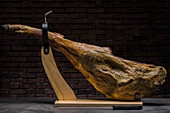 Delicious dry cured Spanish pork leg on wooden holder on gray surface