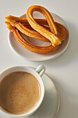 Appetizing churros on plate and cup of fresh morning coffee served on table for breakfast in kitchen