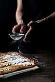 Crop shot of woman covering freshly baked frangipane apple pie with powdered sugar on wooden table