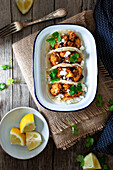From above cauliflower snack tacos in bowl and lemon pieces in plate on wooden table