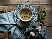 Flat lay of bowls with green pea and coconut cream soup on wooden table with pea pods and garlic in composition