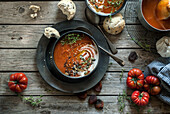 Flat lay of bowls with creamy tomato soup garnished with seeds and served on table with tomatoes and dried apricots