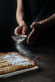 Crop shot of woman covering freshly baked frangipane apple pie with powdered sugar on wooden table