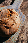 Köstliches frisch gebackenes Brot auf altem Schneidebrett auf einem Holztisch in der Küche von oben