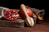 Fresh whole pomegranate and seeds arranged on wooden board near squeezer