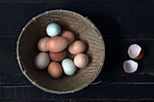 Von oben aufgenommene Weidenschüssel mit rohen Eiern auf Holztisch mit Eierschale daneben