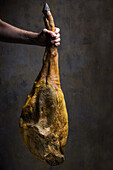 Anonymer Koch zeigt eine große trocken gepökelte iberische Schweinekeule mit goldener Haut bei Tageslicht
