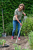 Woman with rake preparing bed for planting pre-grown young plants