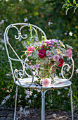 Bouquet of roses, wild carrot, flowering oregano, vetch, autumn anemone and bearded flower on iron chair