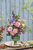 Colorful bouquet of roses (pink), gladioli, fennel blossoms, asparagus, rose hips, autumn anemone, onion blossom in glass vase