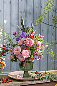 Colourful bouquet of roses (pink), gladioli, fennel blossoms, asparagus, rose hips, autumn anemone, onion blossom in glass vase