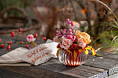 Bouquet of roses (Rosa) and snowberry (Symphoricarpos) 'Amethyst' in vase on garden bench