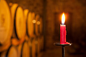 A burning red candle in a wine cellar