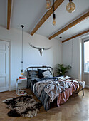 Bedroom with wooden beamed ceiling, metal bed frame and herringbone parquet flooring