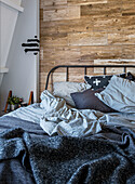 Metal bed in front of wood-panelled wall with striped bed linen, bedspread and cushions