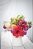 Flower arrangement with red amaryllis (Hippeastrum) and colorful tulips (Tulipa) in a jug