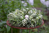 Kräuterkranz mit Rosmarin, Thymian, Nigella und Wiesenkerbel gebunden auf einem Strohrömer, auf Gartentisch