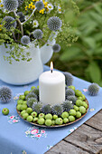 Kranz mit Zieräpfeln, Kugeldisteln (Echinops) und Kerze auf Gartentisch
