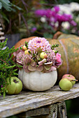 Autumn arrangement with ornamental pumpkin vase, hydrangea blossoms, dahlias, ornamental apples and apples on wooden table