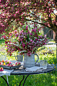 Blumenstrauß aus Zierapfelblüte (Malus) 'Paul Hauber', Brautspiere (Spiraea arguta) und Gräsern auf Gartentisch