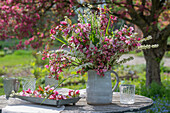 Strauss aus Zierapfel (Malus) 'Paul Hauber', Brautspiere (Spiraea arguta) und Gräsern auf Gartentisch