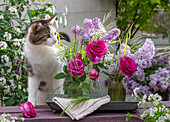 Katze neben Blumensträusschen aus Fliederblüten (Syringa) Rose 'Fräulein Maria', Bärlauchblüten, Waldmeister