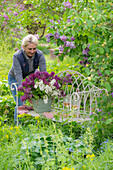 Frau vor Blumenstrauss aus Fliederblüten (Syringa) auf Gartenbank