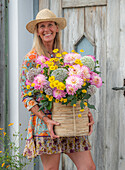 Frau mit sommerlichen Strauß mit Färber-Hundskamille, Dahlie (Dahlia), Zierlauch (Allium) auf der Terrasse