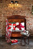 Antiker Vintage-Sessel aus Holz mit roten Akzentkissen und Kerzen vor Backsteinwand