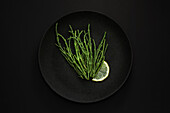 Sea asparagus with lemon wedge on black plate