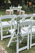 White garden chairs decorated with eucalyptus branches