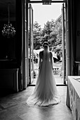 Bride in a long dress stands in front of an open door with a view of the garden