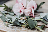 Verlobungsring umgeben von Eukalyptuszweigen und rosa Blüten