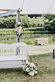 Weiße Vintage-Bank mit Blumendekoration unter einem Zelt im Garten