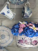 Körbchen mit Blumenmuster gefüllt mit blauen Hortensien und rosa Schafgarbe an rustikaler Holzwand