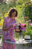 Woman at garden table and colourful bouquet of dahlias (Dahlia), roses (Rosa), autumn anemones (Anemone Hupehensis) and wild carrot