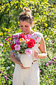 Woman carrying vase with colourful bouquet of dahlias (Dahlia), oriental knotweed (Persicaria orientalis), beard flower (Caryopteris), and borage