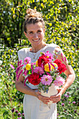 Frau trägt Vase mit buntem Strauß aus Dahlien (Dahlia), orientalischen Knöteriche (Persicaria orientalis), Bartblume (Caryopteris), und Borretsch