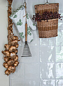 Braid of onions, pot glove with ivy pattern and basket with dried berries on tiled wall