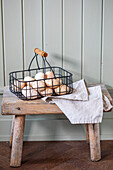 Wire basket with fresh eggs on a rustic wooden stool and tea towel