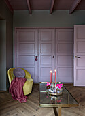 Yellow armchair and glass coffee table in living room with cupboard and door in light purple